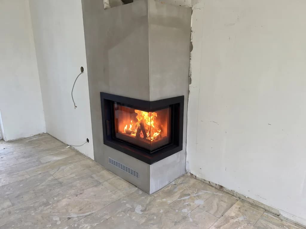 Fertig verputzter und gestrichener Eckkamin mit brennendem Feuer, davor heller Natursteinboden